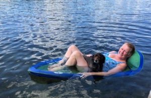 The blogger relaxes on a blue float. There is a black dog in her lap.