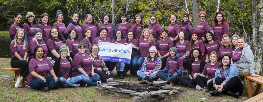 Group photo of women in Girls With Guts t-shirts sitting outside.