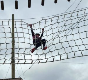 A woman on the high ropes course climbing across a net!