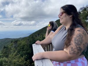 Arielle is on a mountain looking out at the view. She is wearing a pair of red sun glasses. 