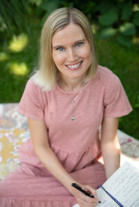 The Blogger has short blond hair. She is wearing a pink shirt.