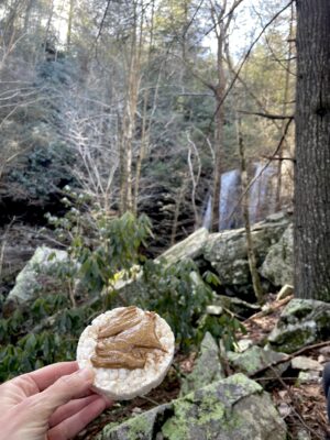 The blogger holds up a rice cake with peanut butter on it.